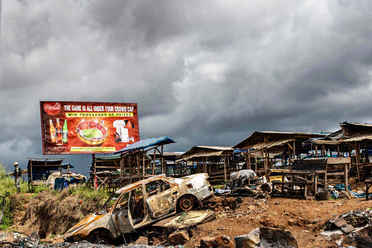 The wreckage of a burnt out car is pictured, allegedly destroyed by separatists fighter in a recent attack, as a Cameroonian soldier (L) patrols the edge of the abandoned market in the majority anglophone South West province in Buea, on Oct. 3, 2018. (Marco Longari/AFP via Getty Images)