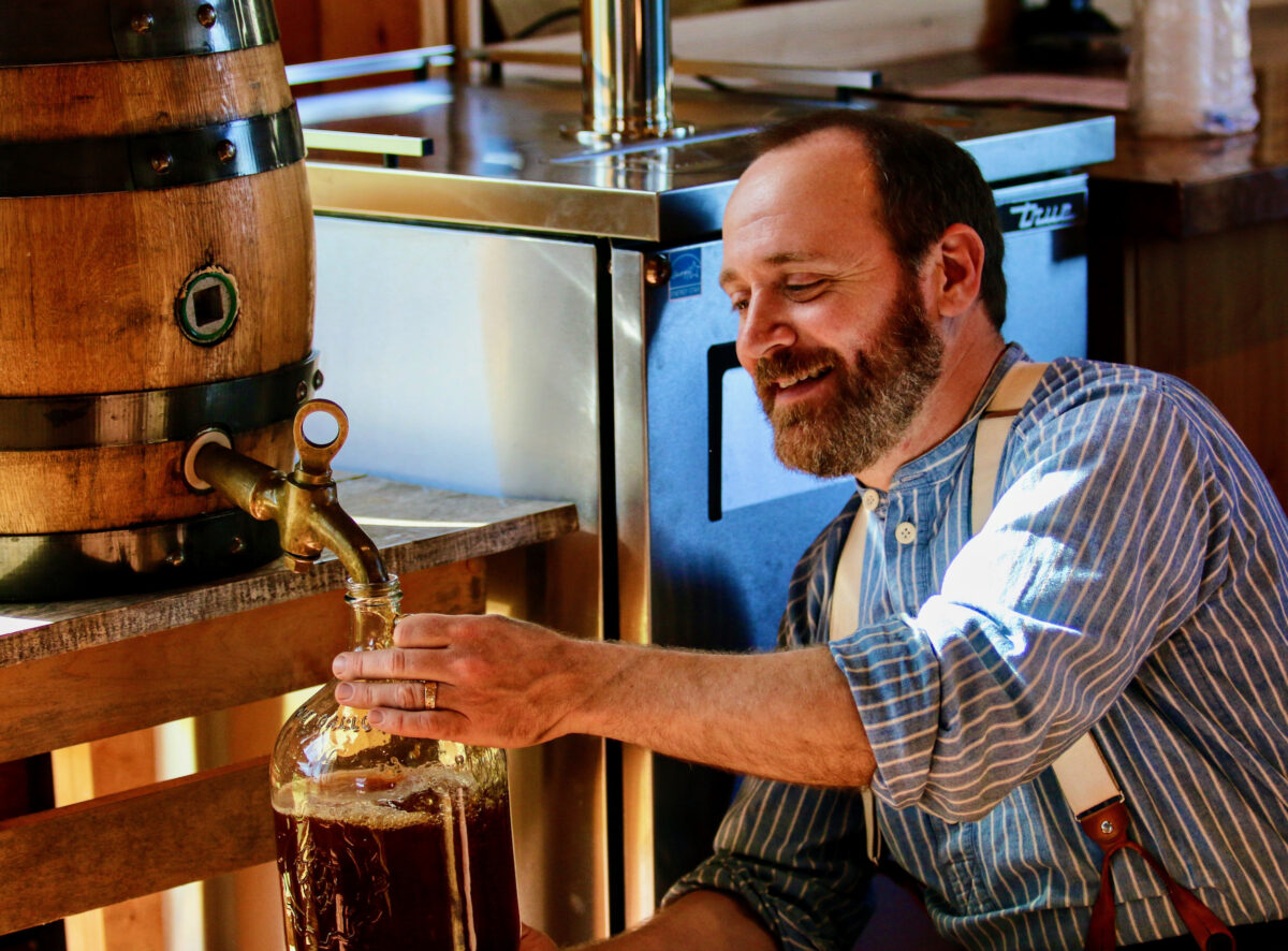 Rob Novak smiles as he taps a keg and fills a bottle of historic beer brewed inside the new Brewhouse on June 3, 2022, at Old World Wisconsin. (Novak is Old World Wisconsin's brewing experience coordinator. (Dean Witter/Wisconsin Historical Foundation)