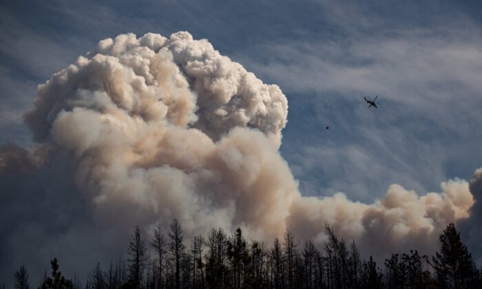 A helicopter carrying a water bucket flies past a pyrocumulus cloud, also known as a fire cloud, produced by the Lytton Creek wildfire burning in the mountains above Lytton, B.C., on August 15, 2021. (The Canadian Press/Darryl Dyck)