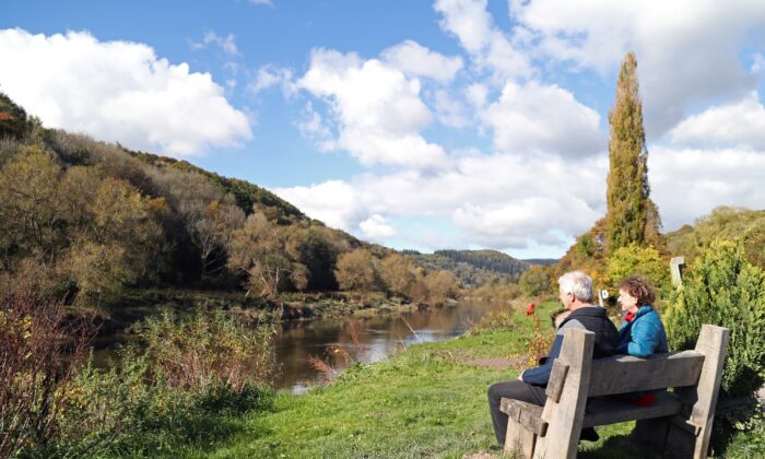 A couple sit on a bench looking out across the River Wye towards Wales, from the village of Brockweir, western England, on Oct. 15, 2020 (Geoff Caddick /AFP via Getty Images)
