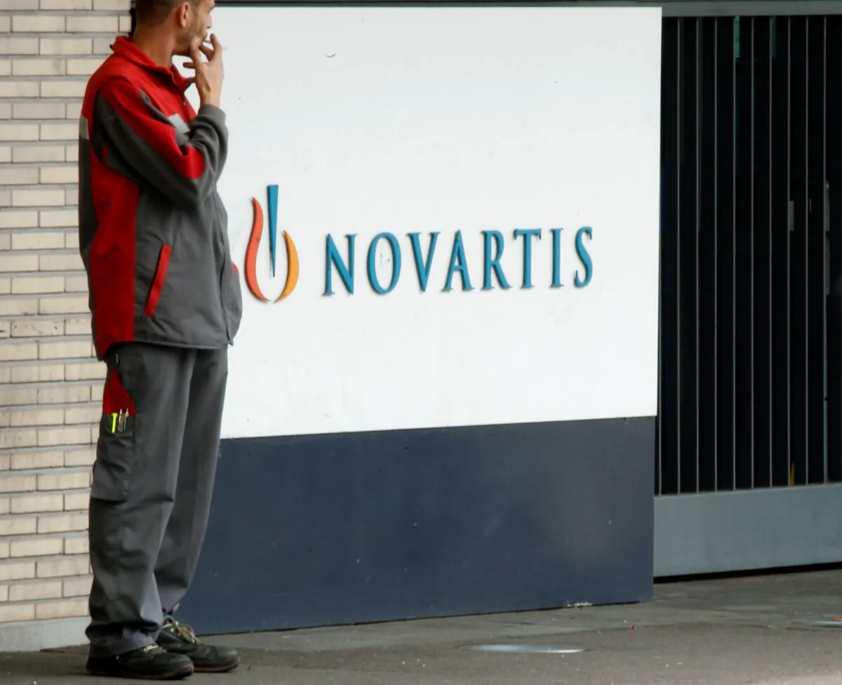 An employee smokes a cigarette beside the logo of Swiss drugmaker Novartis AG in front of a plant in Basel on Oct. 25, 2011. (Arnd Wiegmann/Reuters)