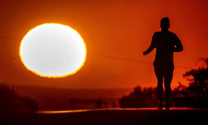 A man runs up a hill as the sun rises on June 17, 2022. (AP Photo/Michael Probst)