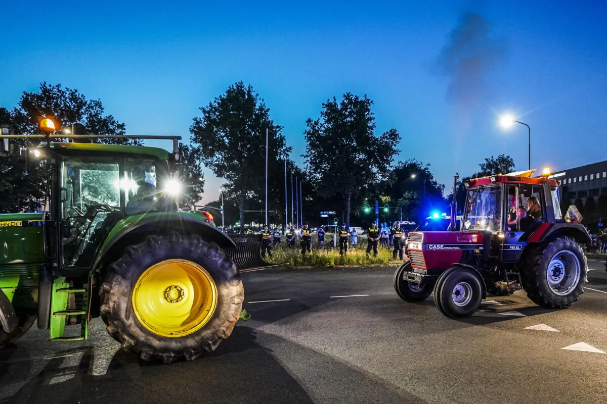 Tractors drive by Dutch police officers standing guard as dutch police close access to Apeldoorn on the A1 highway to stop potential farmers demonstrating against the Dutch government's plans to cut nitrogen emissions, on 29 June 2022. (JEROEN JUMELET/ANP/AFP via Getty Images)