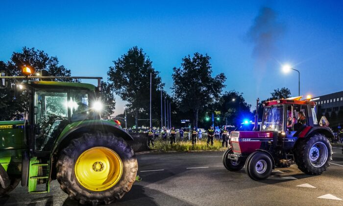 Tractors drive by Dutch police officers standing guard as dutch police close access to Apeldoorn on the A1 highway to stop potential farmers demonstrating against the Dutch government's plans to cut nitrogen emissions, on 29 June 2022. (JEROEN JUMELET/ANP/AFP via Getty Images)