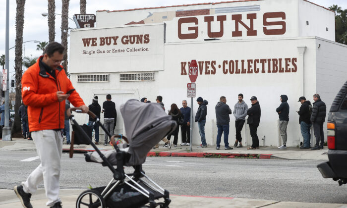 2020 年 3 月 15 日，当人们在加利福尼亚州卡尔弗城的 Martin B. Retting, Inc. 枪支商店外排队时，一名男子推着婴儿车走路。（Mario Tama/Getty Images/TNS）