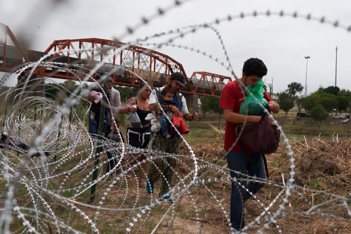Illegal immigrants who crossed the Rio Grande River walk along concertina wire in Eagle Pass, Texas, on May 22, 2022. (Allison Dinner/AFP via Getty Images)