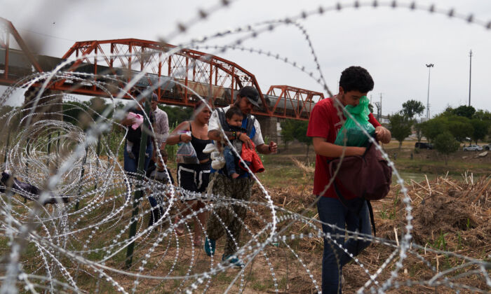 Illegal immigrants who crossed the Rio Grande River walk along concertina wire in Eagle Pass, Texas, on May 22, 2022. (Allison Dinner/AFP via Getty Images)
