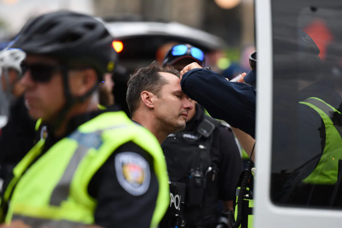 A police officer receives treatment after four people were arrested in a demonstration in downtown Ottawa on June 30, 2022. (The Canadian Press/Spencer Colby)
