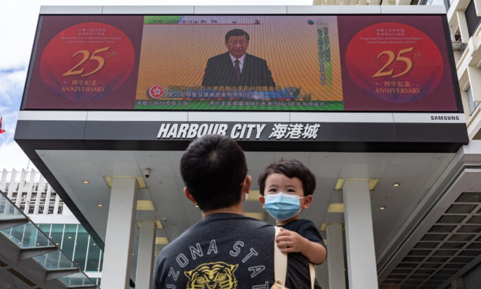 A man holding a child walks in front of a screen showing a live broadcast of Chinese leader Xi Jinping speaking during a swearing-in ceremony for Hong Kong's new chief executive, John Lee, on July 1, 2022, in Hong Kong, China. Hong Kong celebrates the 25th anniversary of its handover from Britain to China on July 1. (Anthony Kwan/Getty Images)