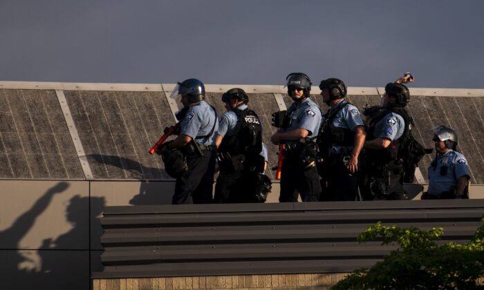 Police officers stand on the roof of the Third Police Precinct as one launches an explosive projectile down on the protesters below in Minneapolis on May 27, 2020. (Stephen Maturen/Getty Images)