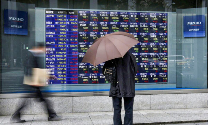 A man holding an umbrella looks at an electronic stock quotation board outside a brokerage in Tokyo, Japan, on April 7, 2015. (Issei Kato/Reuters)