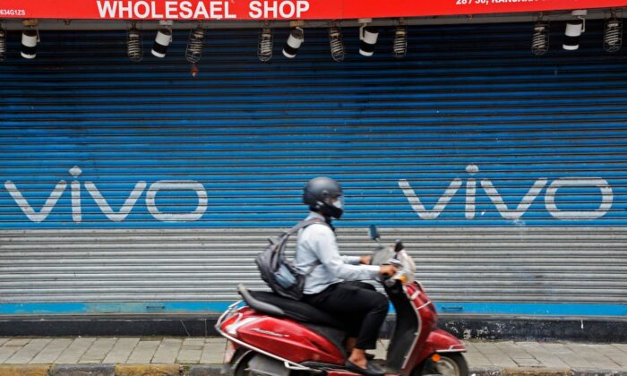 A scooterist rides past an advertisement of Chinese mobile phone maker Vivo, painted on a shuttered shop of a market in Mumbai on July 31, 2020. (Indranil Mukherjee/AFP via Getty Images)