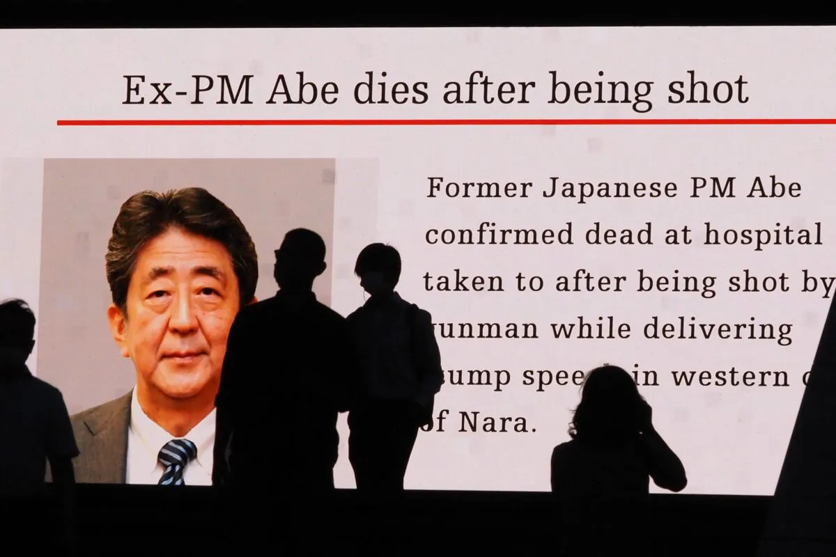 Pedestrians are silhouetted against a large public video screen showing an image of former Japanese Prime Minister Shinzo Abe in the Akihabara district of Tokyo, Japan, on July 8, 2022. Abe was shot and killed in the city of Nara. (Toshifumi Kitamura/AFP via Getty Images)