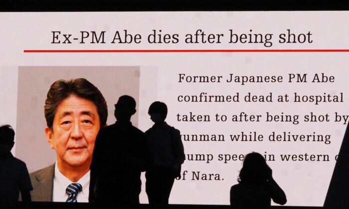 Pedestrians are silhouetted against a large public video screen showing an image of former Japanese Prime Minister Shinzo Abe in the Akihabara district of Tokyo, Japan, on July 8, 2022. Abe was shot and killed in the city of Nara. (Toshifumi Kitamura/AFP via Getty Images)