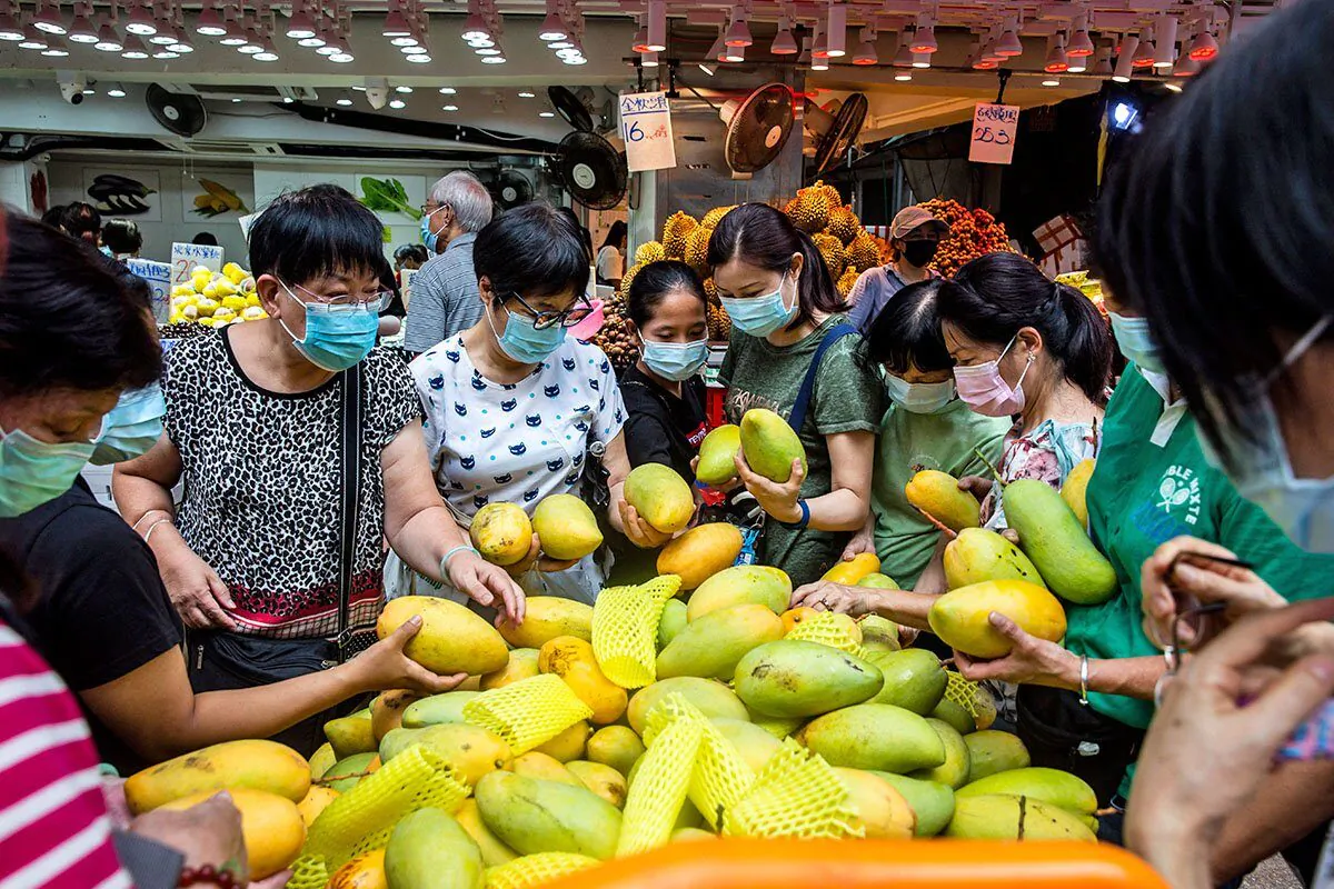 People buying mangoes at a fruit stall in Hong Kong. The Hong Kong government said on July 6, 2022, that the mangoes imported from Taiwan tested positive for COVID-19, and has ordered vendors to stop selling them and to destroy them all.  (Isaac Lawrence/AFP)