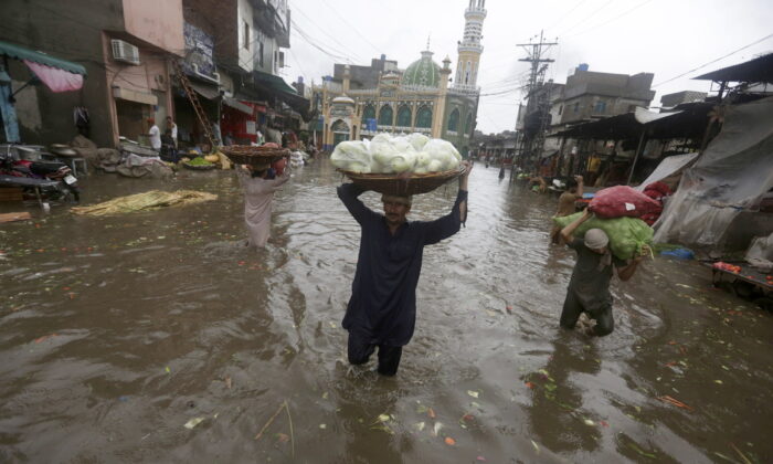 2022 年 7 月 21 日，星期四，巴基斯坦拉合尔，大雨过后，工人们在水淹的道路上跋涉时搬运农产品。（美联社照片/KM Chaudary）