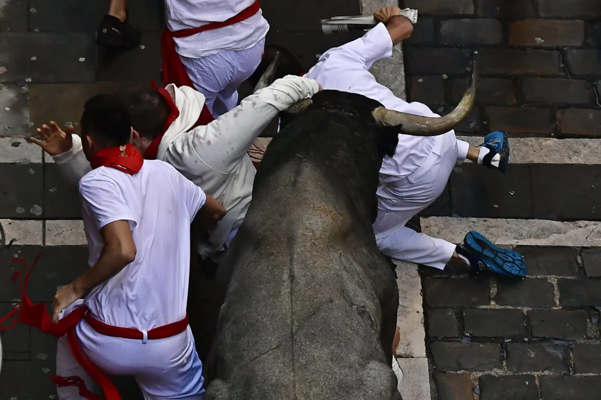 Runners fall as people run in the street with fighting bulls during the running of the bulls at the San Fermin Festival in Pamplona, northern Spain, on July 9, 2022. (Alvaro Barrientos/AP Photo)