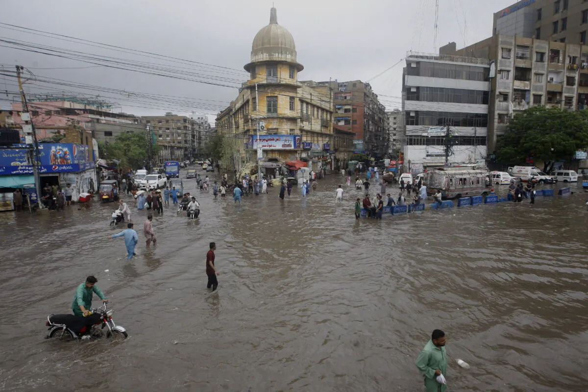 Motorcyclists and people wade through a flooded road in a business district after a heavy rainfall in Karachi, Pakistan, on July 9, 2022. (Fareed Khan/AP Photo)