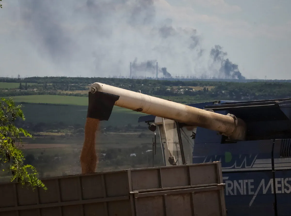 Farmers harvest wheat as Vuhlehirsk's heat power plant burns in the distance after a shelling, amid Russia's attack on Ukraine, in the Donbas region, Ukraine July 13, 2022. REUTERS/Gleb Garanich