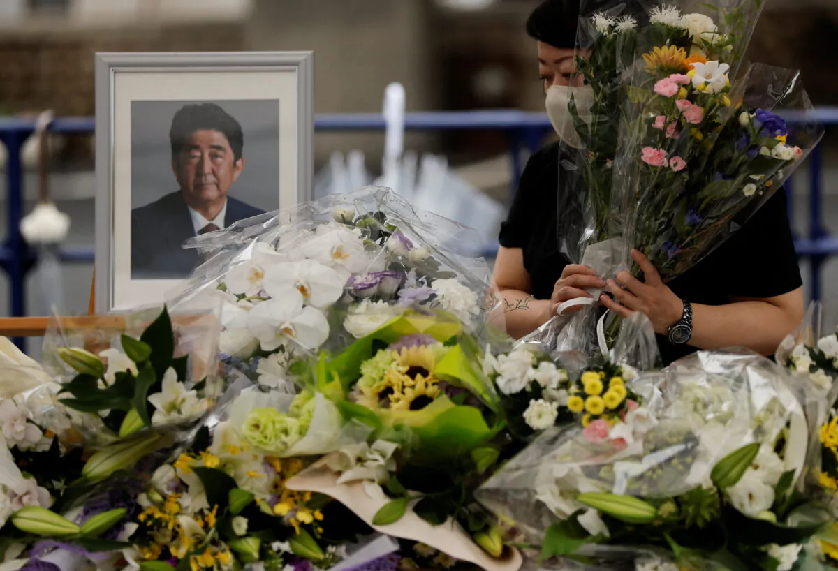 A mourner offers flowers next to a picture of late former Japanese Prime Minister Shinzo Abe, who was shot while campaigning for a parliamentary election, on the day to mark a week after his assassination at the Liberal Democratic Party headquarters, in Tokyo on July 15, 2022. (Issei Kato/Reuters)