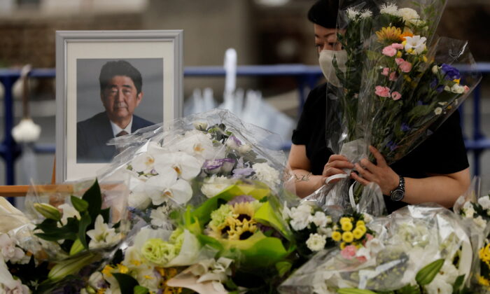 A mourner offers flowers next to a picture of late former Japanese Prime Minister Shinzo Abe, who was shot while campaigning for a parliamentary election, on the day to mark a week after his assassination at the Liberal Democratic Party headquarters, in Tokyo on July 15, 2022. (Issei Kato/Reuters)