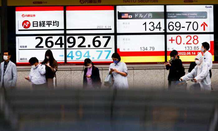 Passersby are seen in front of a screen displaying the Japanese yen exchange rate against the U.S. dollar and Nikkei share average in Tokyo, Japan, on June 14, 2022. (Issei Kato/Reuters)