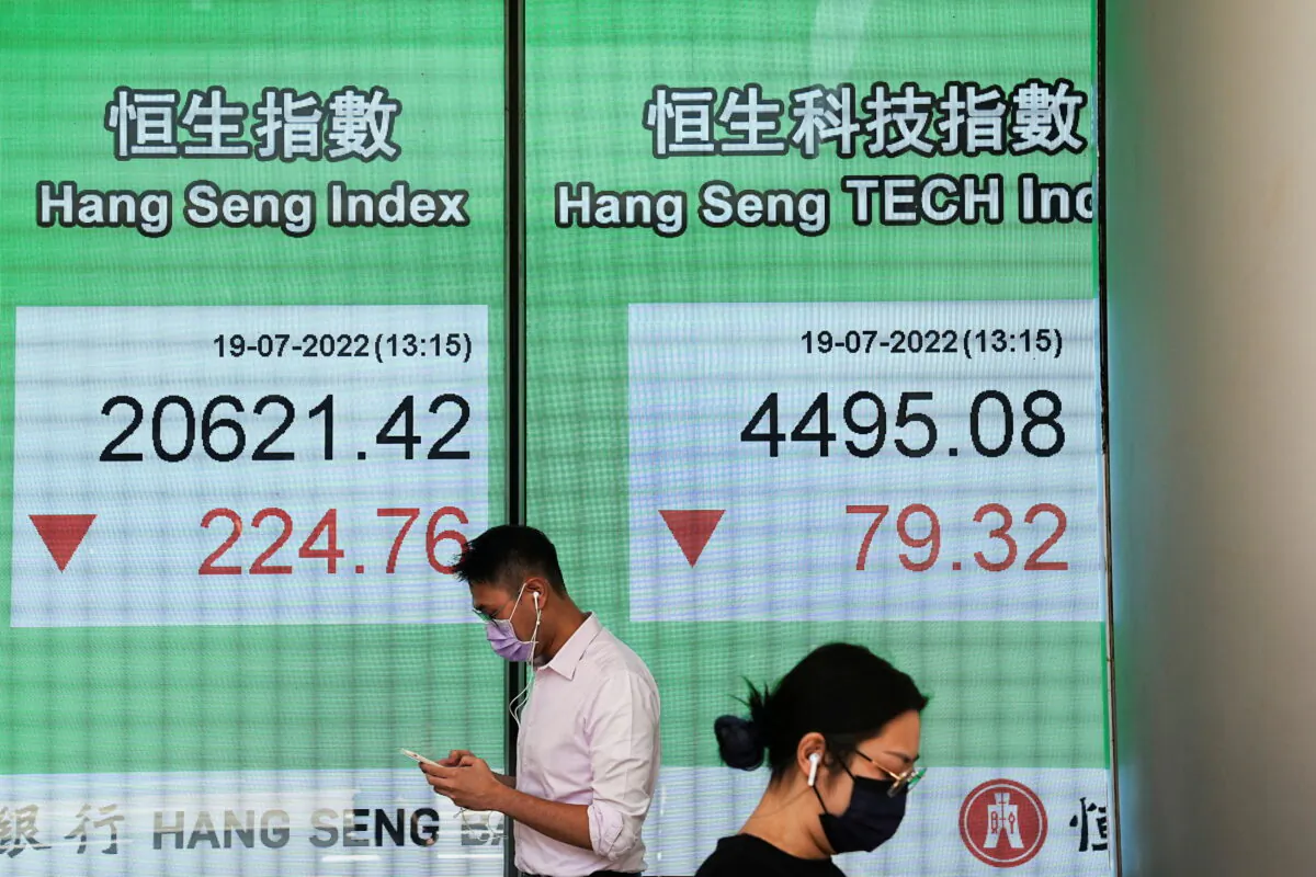 People walk past a screen displaying the Hang Seng stock index at Central district in Hong Kong on July 19, 2022. (Lam Yik/Reuters)