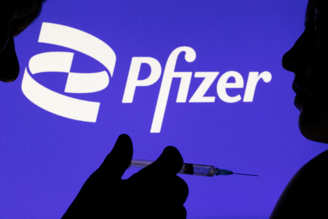 A person poses with a syringe in front of the Pfizer Inc. logo on Dec. 11, 2021. (Dado Ruvic/Reuters)