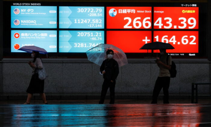 Passersby wearing protective face masks walk in front of an electronic board showing Japan's Nikkei share average, amid the coronavirus disease (COVID-19) pandemic, in Tokyo, Japan, on July 14, 2022. (Issei Kato/Reuters)