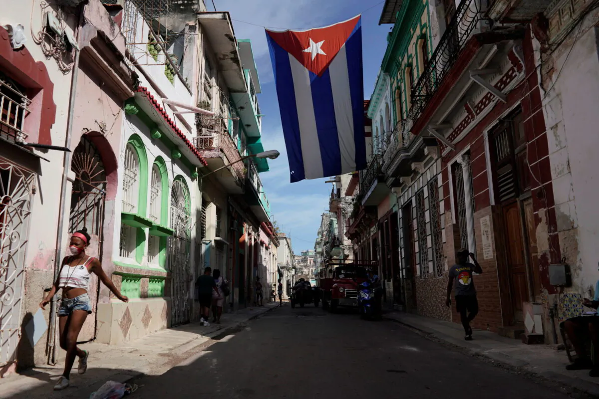 People walk under a Cuban flag hanging in downtown Havana, Cuba, on Oct. 8, 2021. (Alexandre Meneghini/Reuters)