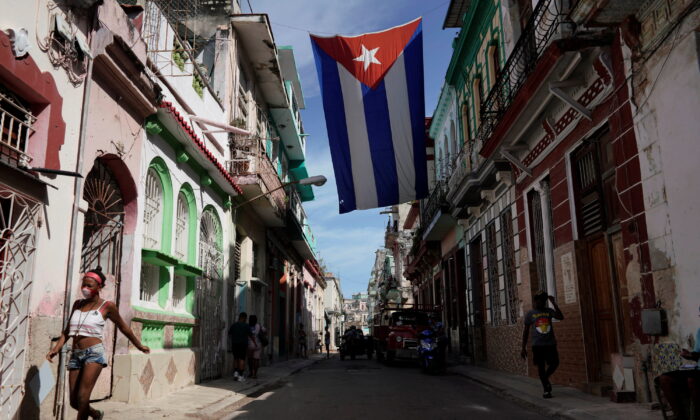People walk under a Cuban flag hanging in downtown Havana, Cuba, on Oct. 8, 2021. (Alexandre Meneghini/Reuters)