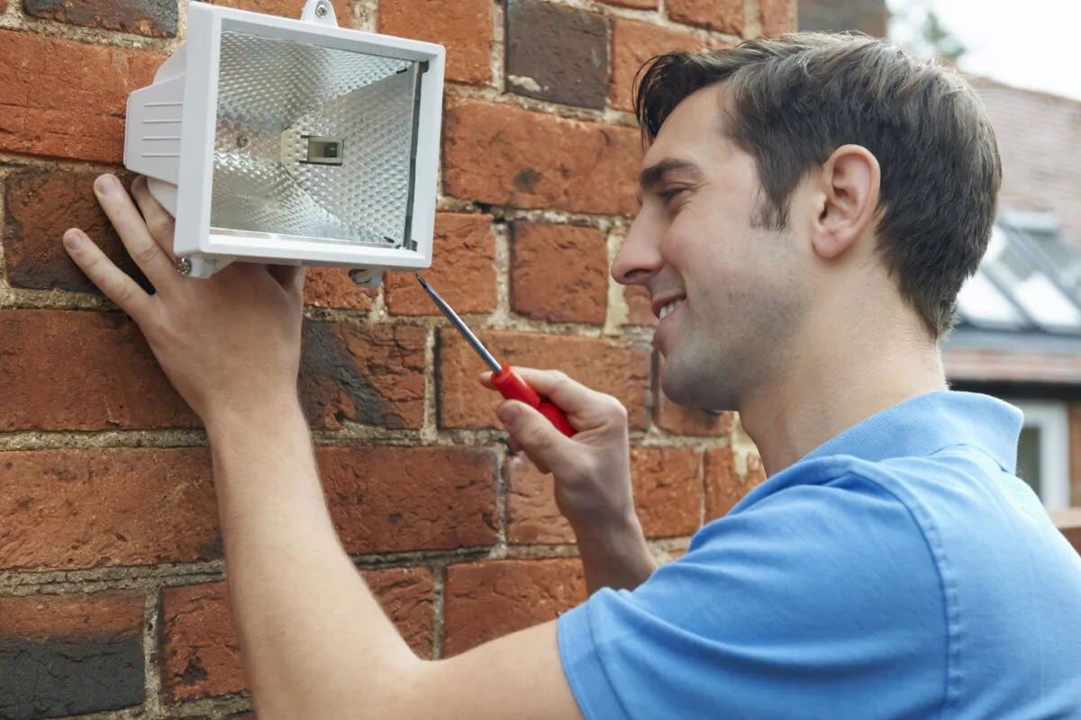 Man Fitting Security Light To House Wall (SpeedKingz/Shutterstock)