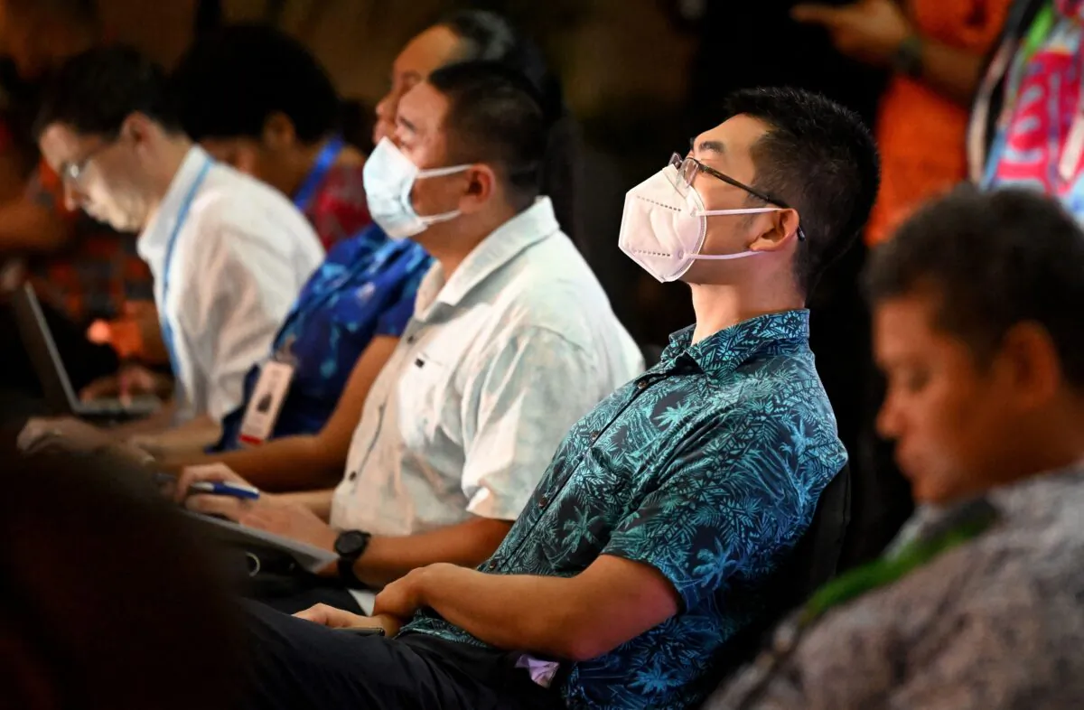 Two officials from the Chinese Embassy (2/R) and (C) listen to US Vice-President Kamala Harris speak via video-link to the Pacific Islands Forum (PIF) in Suva, Fiji, on July 13, 2022. (WILLIAM WEST/AFP via Getty Images)
