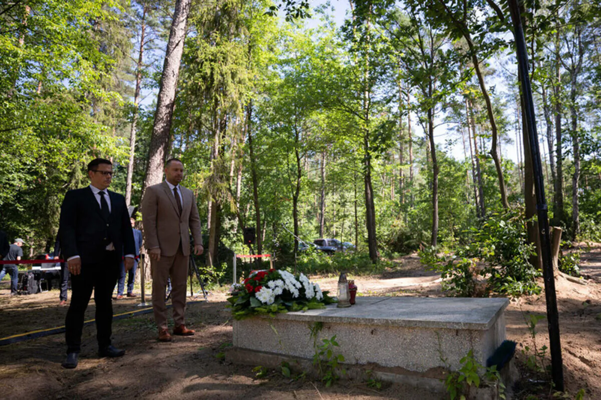 Karol Nawrocki, right, head of the Institute of National Remembrance (IPN), stands in front of a grave as he meets the media near Działdowo, Poland, Wednesday, July 13, 2022. (Mikolaj Bujak/Institute of National Remembrance via AP)