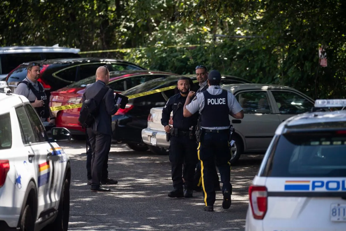 RCMP and Surrey police officers work at the scene of a shooting near a red Tesla vehicle, back, in Surrey, B.C., on July 14, 2022. (The Canadian Press/Darryl Dyck)