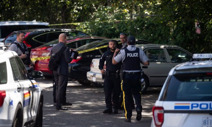 RCMP and Surrey police officers work at the scene of a shooting near a red Tesla vehicle, back, in Surrey, B.C., on July 14, 2022. (The Canadian Press/Darryl Dyck)