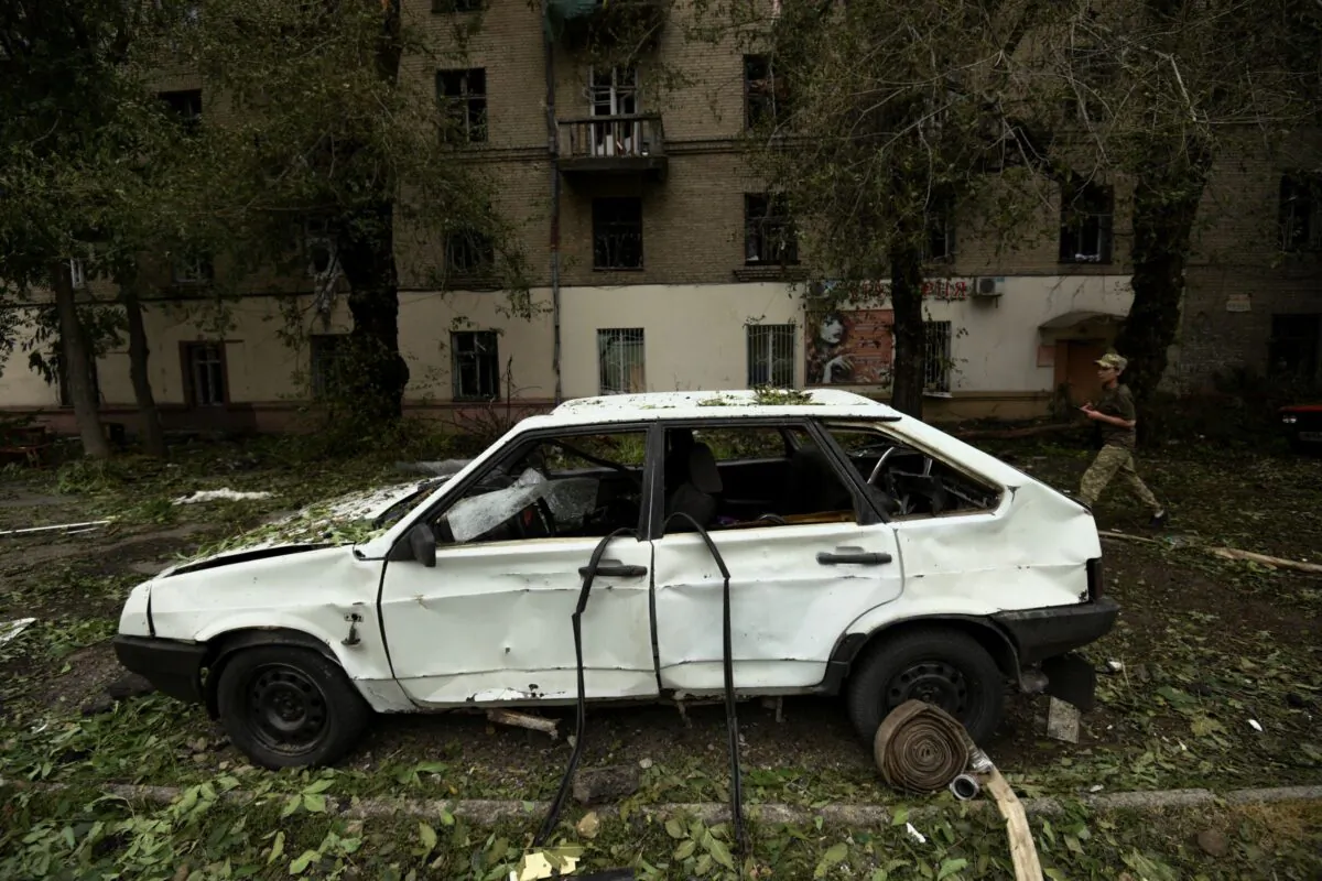 A Ukrainian servicewoman walks past a car damaged by a Russian missile strike in Dnipro, Ukraine, on July 16, 2022. (Mykola Synelnykov/Reuters)