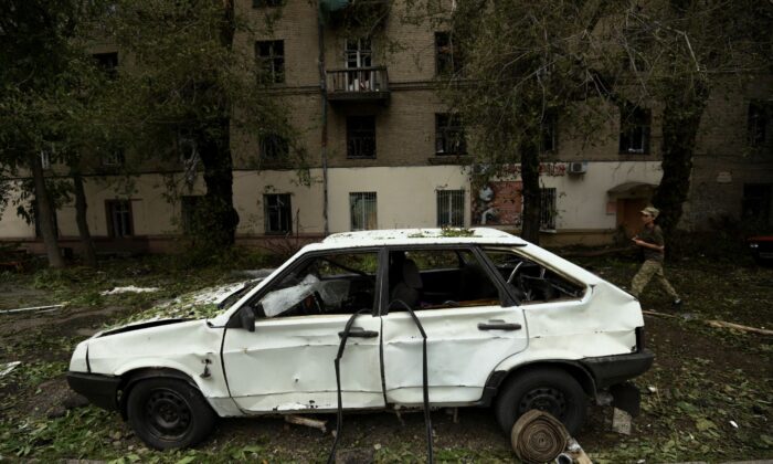 A Ukrainian servicewoman walks past a car damaged by a Russian missile strike in Dnipro, Ukraine, on July 16, 2022. (Mykola Synelnykov/Reuters)