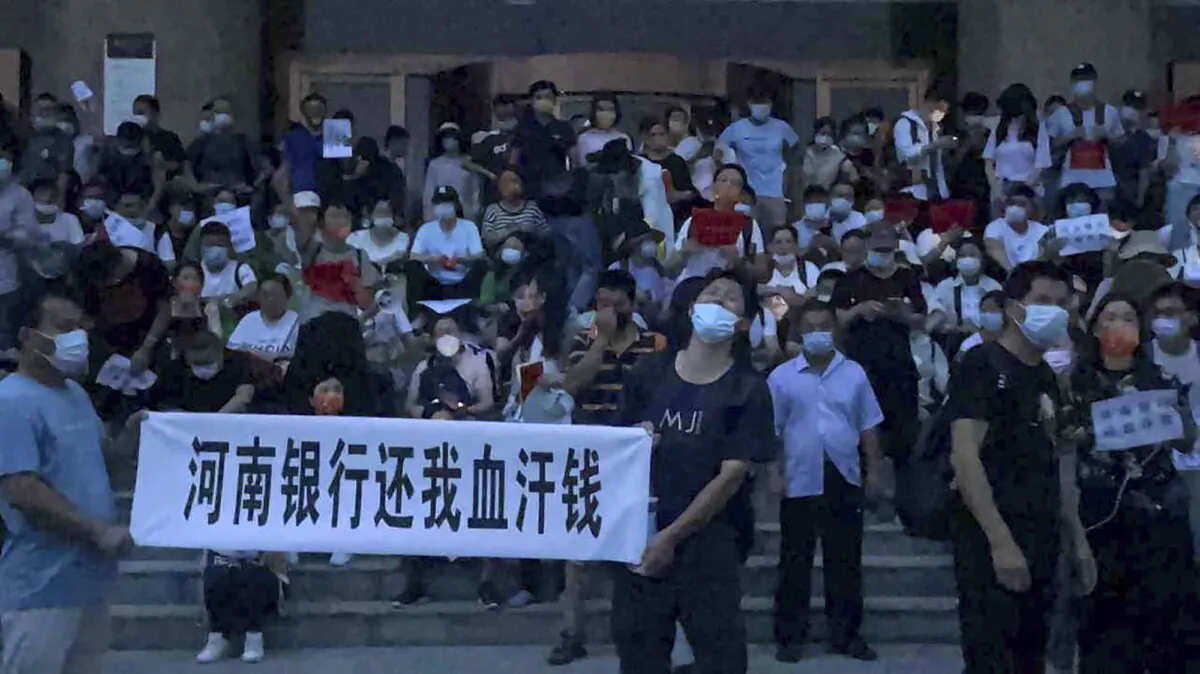 People hold banners and chant slogans to stage a protest at the entrance to a branch of China's central bank in Zhengzhou, in central China's Henan Province, on July 10, 2022. A large crowd of angry Chinese bank depositors faced off with police on July 10, some reportedly injured as they were roughly taken away. This case has drawn attention because of earlier attempts to use a COVID-19 tracking app to prevent them from mobilizing. (Yang/AP Photo)