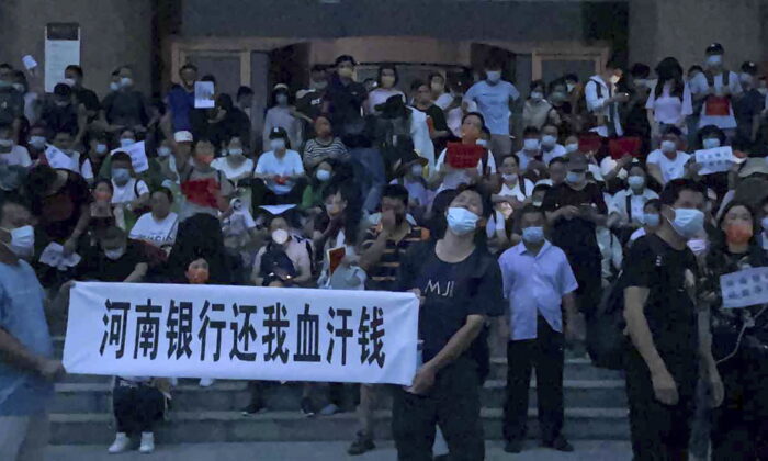 People hold banners and chant slogans to stage a protest at the entrance to a branch of China's central bank in Zhengzhou, in central China's Henan Province, on July 10, 2022. A large crowd of angry Chinese bank depositors faced off with police on July 10, some reportedly injured as they were roughly taken away. This case has drawn attention because of earlier attempts to use a COVID-19 tracking app to prevent them from mobilizing. (Yang/AP Photo)