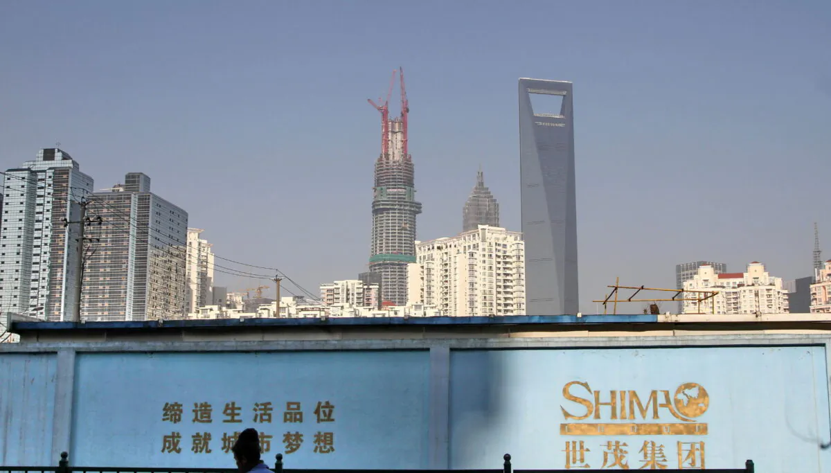 A man walks past a wall carrying the logo of Shimao Group, with residential buildings and the financial district of Pudong seen in the background, in Shanghai, on Jan. 1, 2013. (Stringer/Reuters)