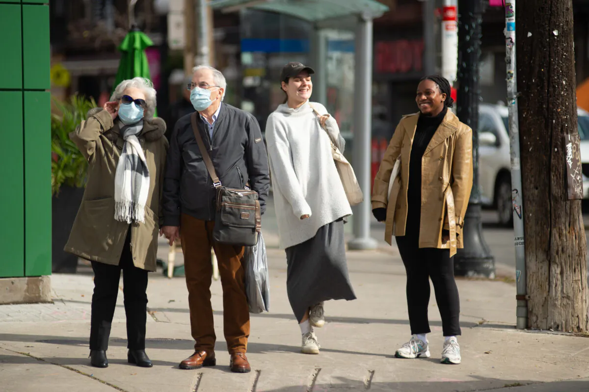 An elderly couple wearing masks wait to cross Ossington St. next to two unmasked younger women, Toronto, on Oct. 28, 2021. (The Canadian Press/Eduardo Lima)