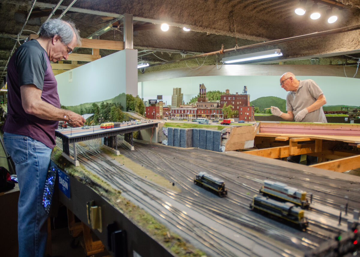 Allan Winter (L) works on the electrical portion of the recreation of the Allentown, Pa., train station, and Alan Alcabes paints its scenery, at the West Island Model Railroad Club on Long Island, N.Y. (Dave Paone/The Epoch Times)