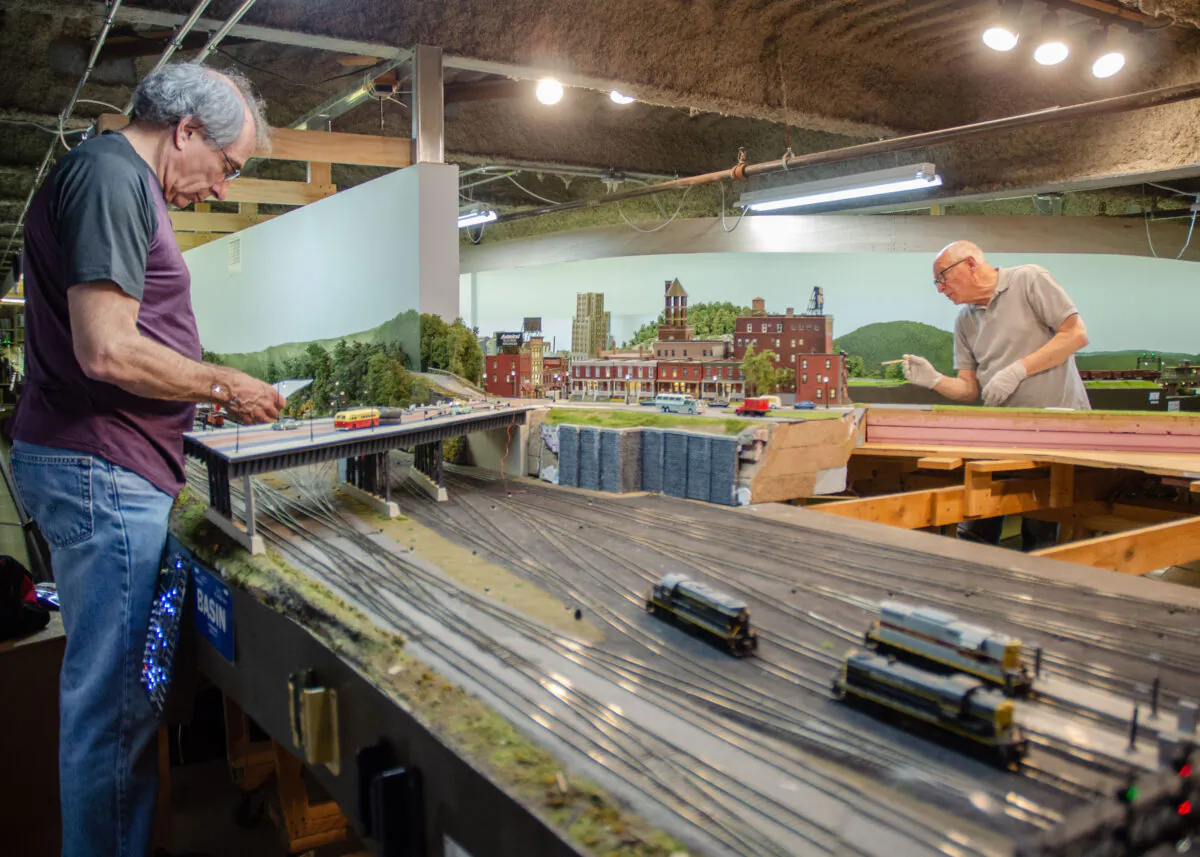Allan Winter (L) works on the electrical portion of the recreation of the Allentown, Pa., train station, and Alan Alcabes paints its scenery, at the West Island Model Railroad Club on Long Island, N.Y. (Dave Paone/The Epoch Times)