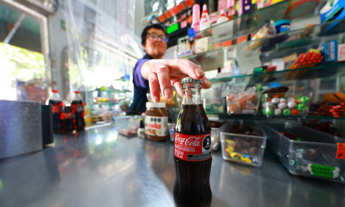 2022 年 6 月 3 日，一名女售货员拿着可口可乐通过墨西哥城的价格阅读器。（Hector Vivas/Getty Images）