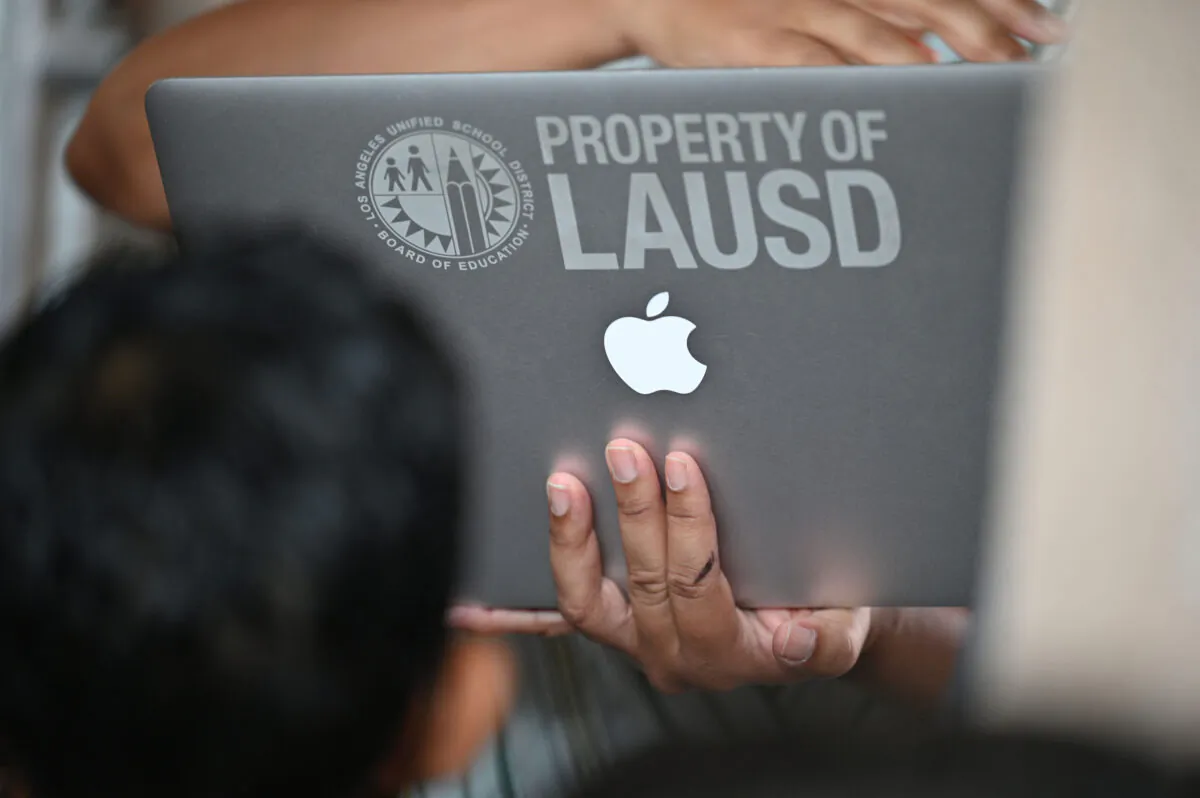 A school administrator confirms student health check data on a laptop computer as students and parents wait in line to enter school at Grant Elementary School in Los Angeles on Aug. 16, 2021. (Robyn Beck/AFP via Getty Images)