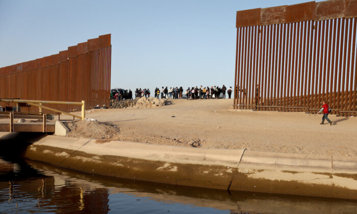 Illegal immigrants near a gap in the U.S.-Mexico border barrier, awaiting processing by the U.S. Border Patrol in Yuma, Arizona, on May 20, 2022. (Mario Tama/Getty Images)