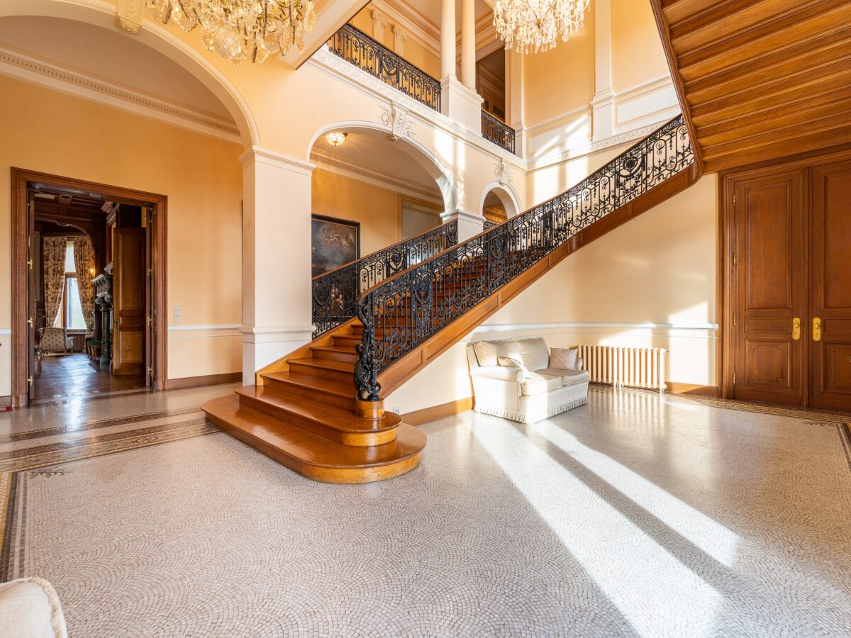 The grand entry hall features a stunning staircase leading to the bedrooms, suites, and apartments on the upper floors. (Courtesy of Belgium Sotheby’s International Realty)
