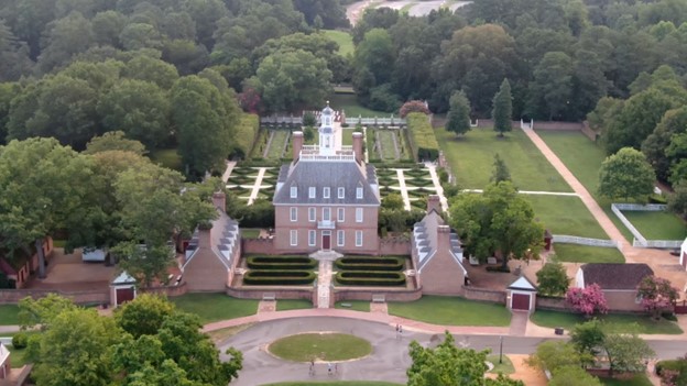This aerial view of the Governor's Palace reveals the front court, side yards, and formal garden at the rear, and is surrounded by groomed lawns and trees. The Palace was designed in a renaissance style that was popular in England and the Virginia Colony. The symmetrical composition is displayed by the ordered and proportioned placement of windows, doors, and central tower. The restrained use of ornament and rubbed red brick give the appearance of a strong masculine building. (J.H. Smith/Cartio)