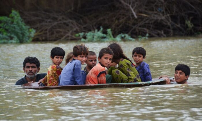 A man (L) along with a youth use a satellite dish to move children across a flooded area after heavy monsoon rainfalls in Jaffarabad district, Balochistan Province, Pakistan, on Aug. 26, 2022. (Fida Hussain/AFP via Getty Images)